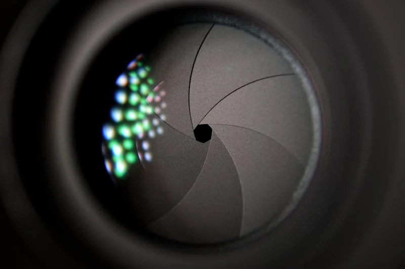 Close-up of a camera aperture, its blades opening around a point of light