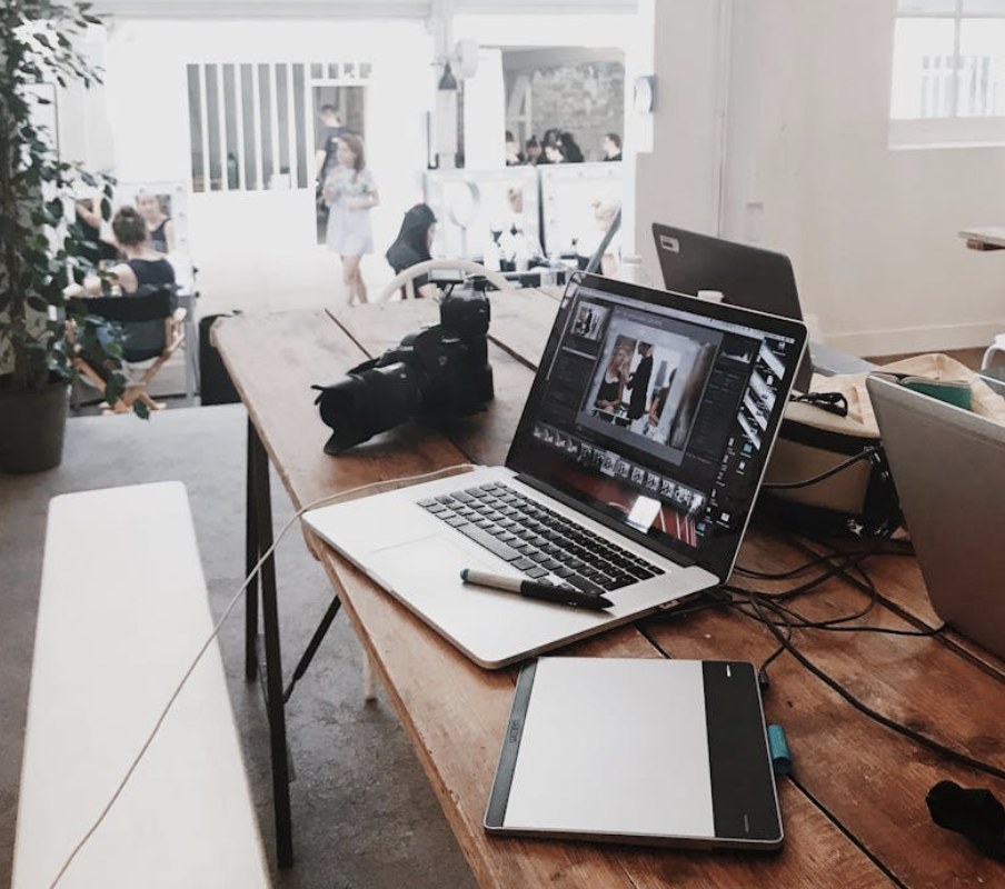A studio workspace with a laptop, camera and drawing tablet on a long wooden table